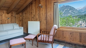 A wooden cabin interior with a sofa, two chairs, a radiator, and a window with a mountain view. - Feleit 9 (Bormio)