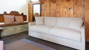 A beige sofa with a stone wall and wooden paneling in the background. - Feleit 9 (Bormio)