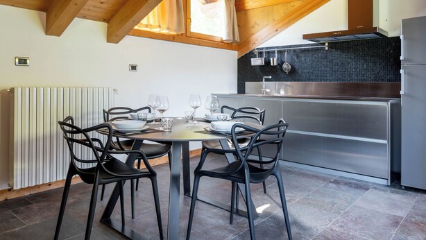 A modern kitchen with a dining area, featuring a round table, black chairs, and a stainless steel refrigerator. - Feleit 9 (Bormio)