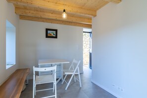A room with a wooden ceiling, a white desk, two white chairs, a small painting, and a window.