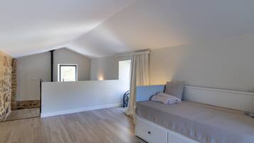 Une chambre avec un lit, une fenêtre, un ventilateur et un mur en pierre.