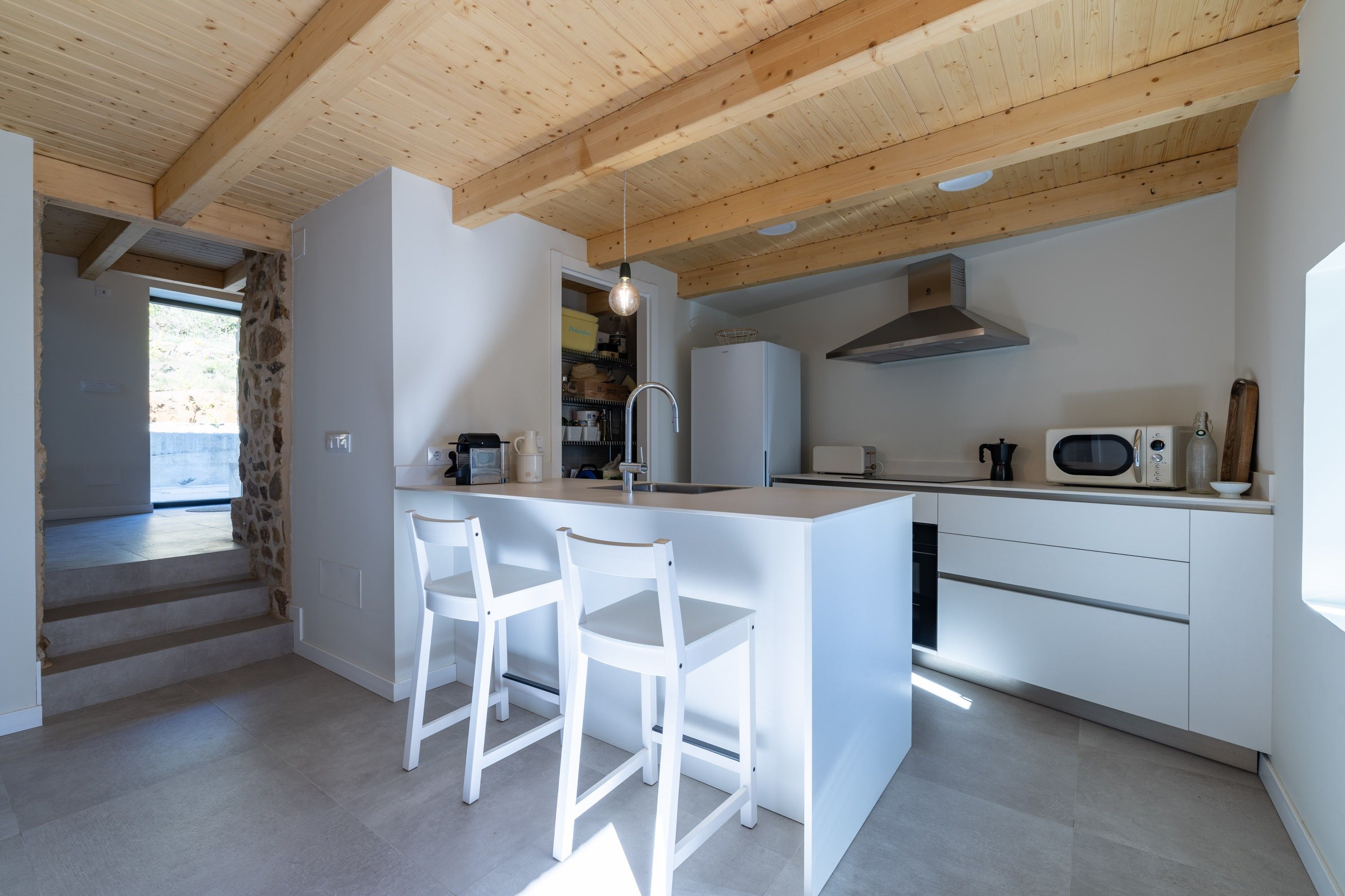 Een moderne keuken met witte kasten, een centraal eiland met barstoelen, een inbouwoven en een roestvrijstalen afzuigkap.