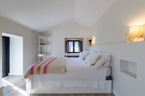A bedroom with a bed, a window, a shelf, and a wall-mounted lamp.