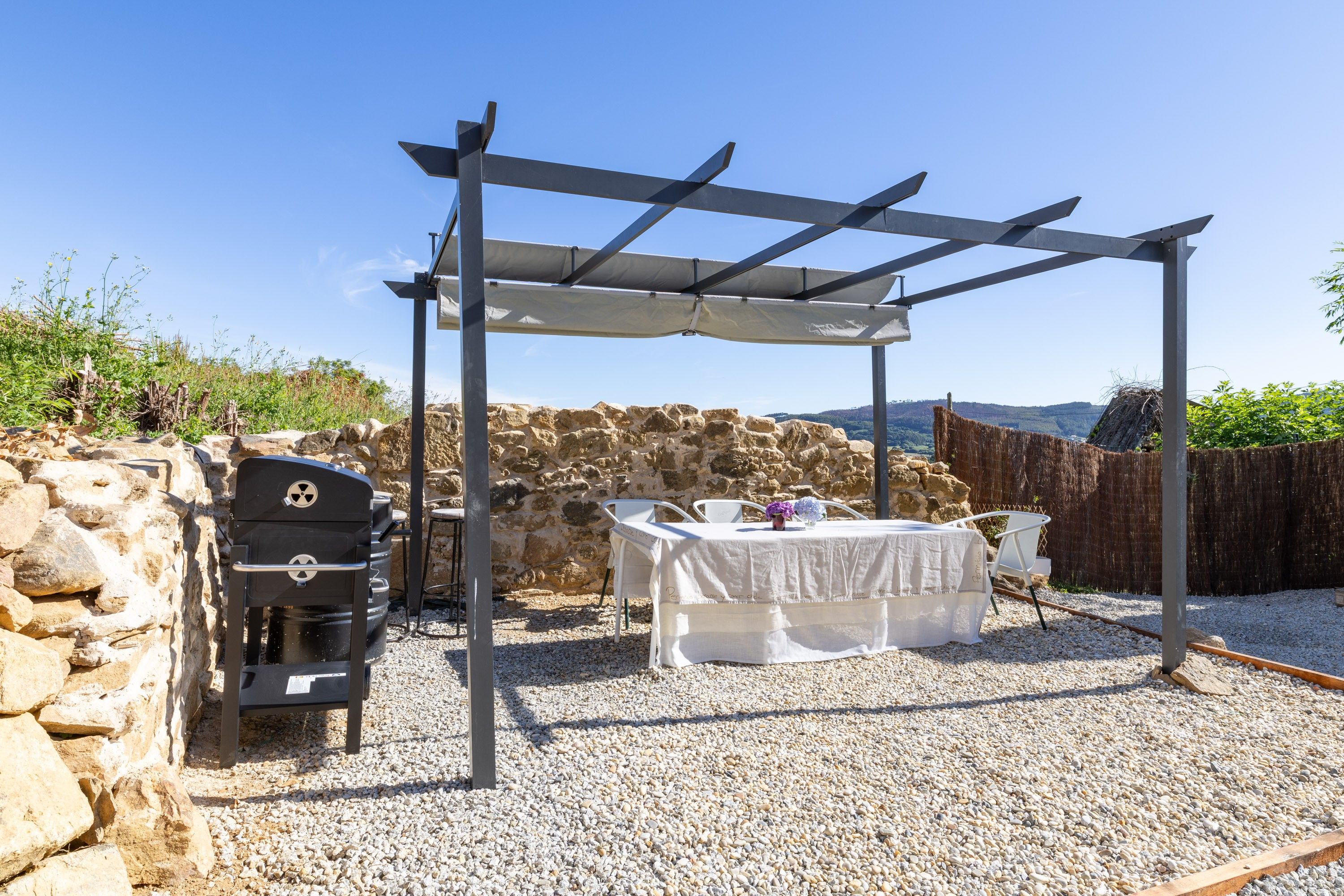 Een terras buiten met een barbecue, een eettafel en een pergola die schaduw biedt.