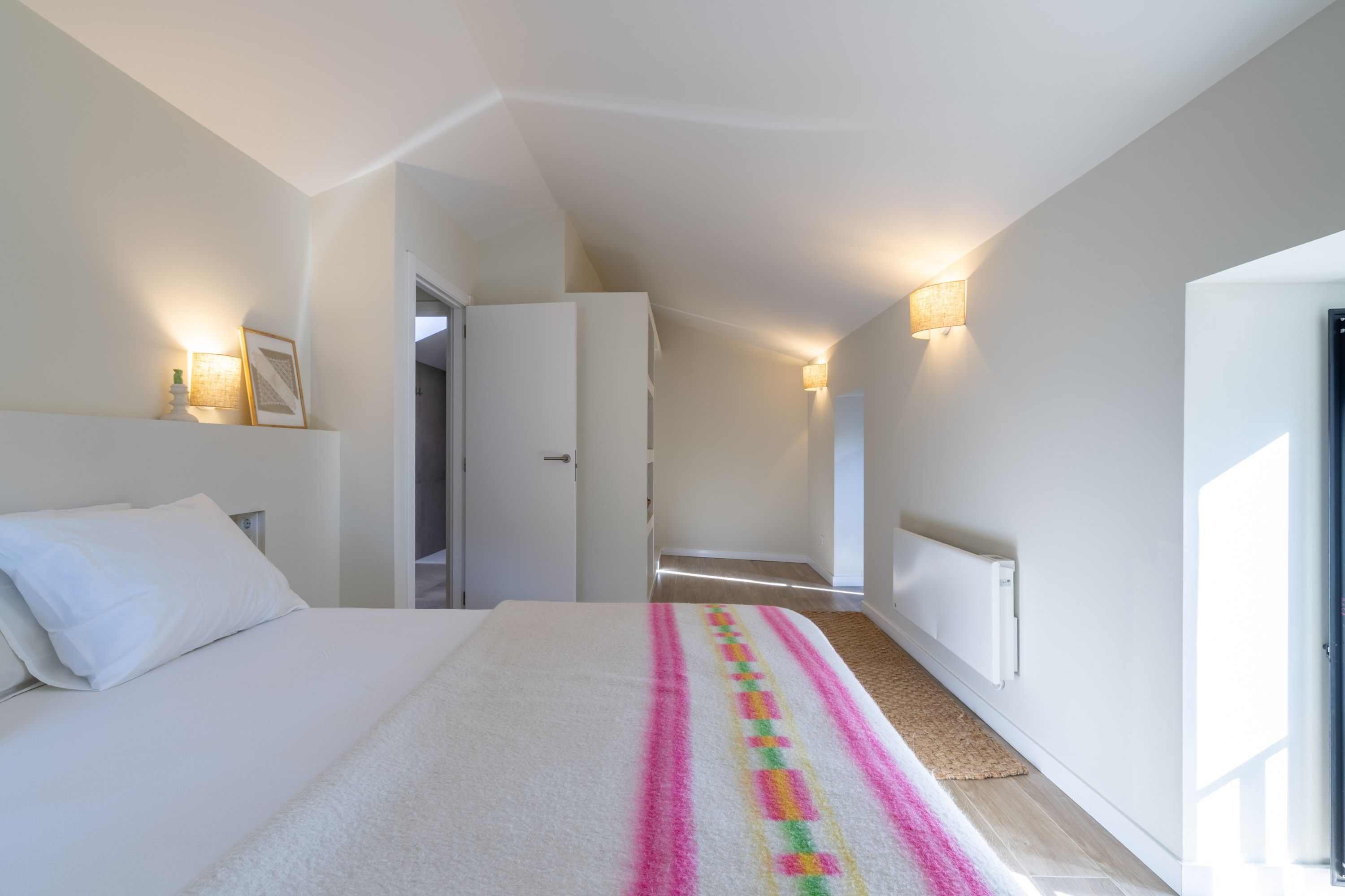 Een hotelkamer met een bed, een gang die naar een deur leidt en een radiator.