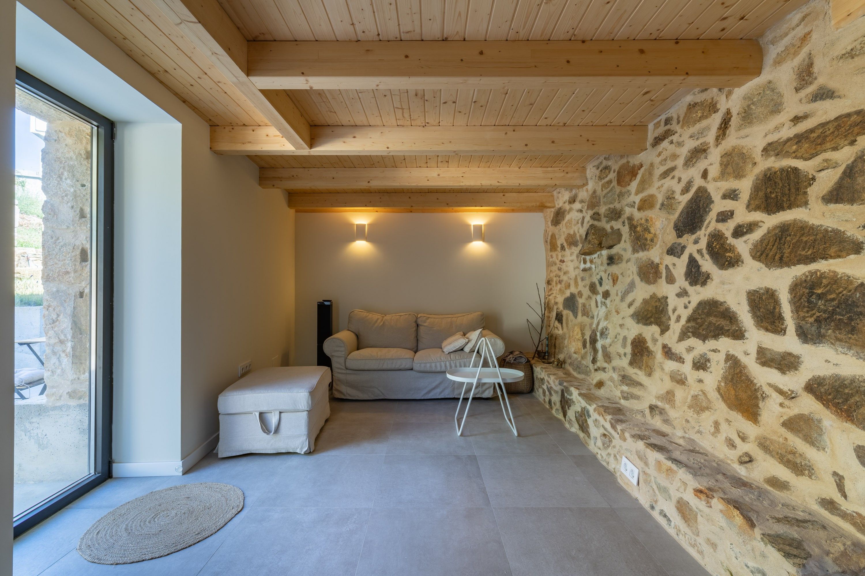 Ein gemütliches Zimmer mit Steinwand, einer Couch, einem kleinen Tisch und einem Fenster.