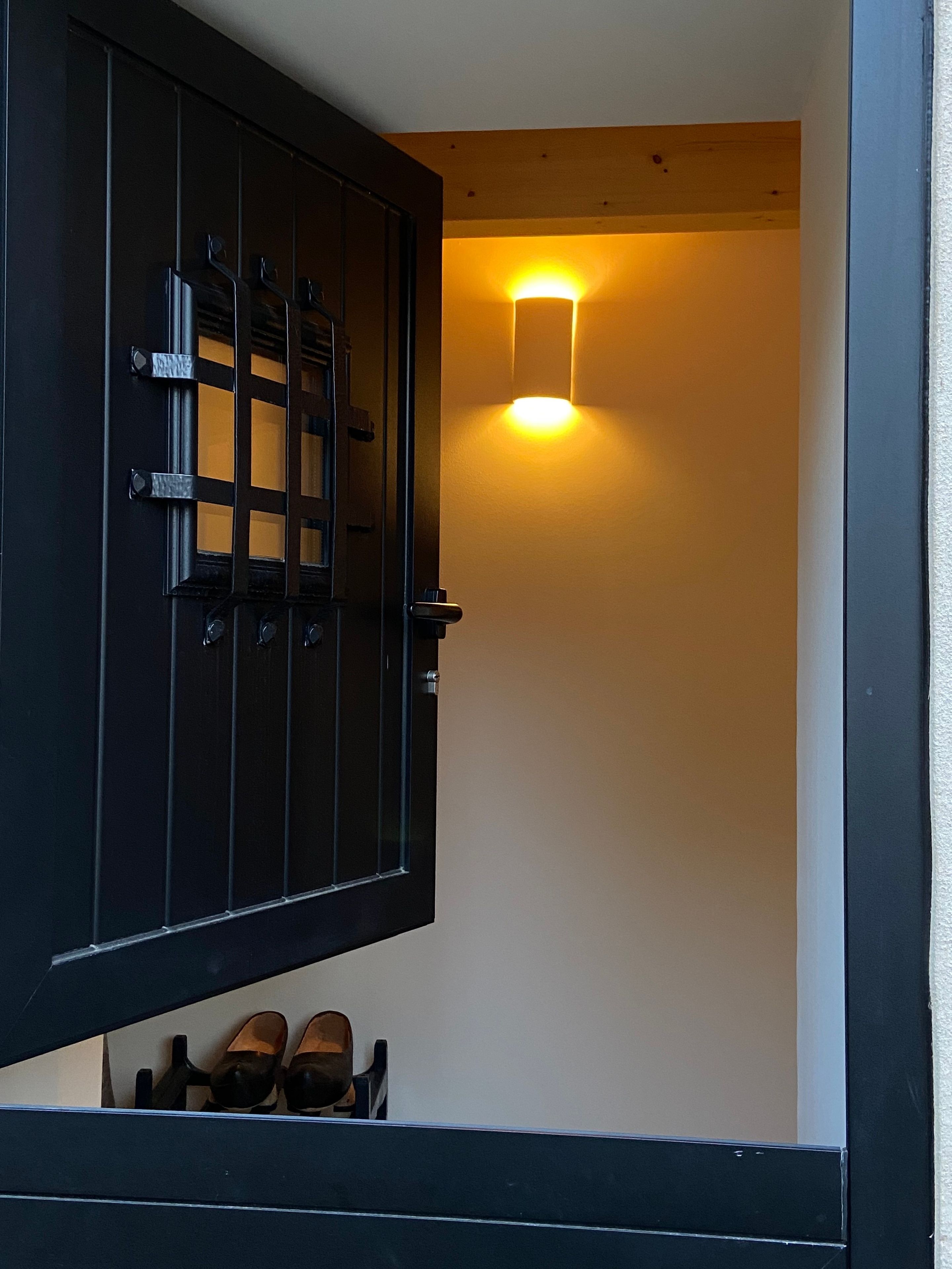 Une porte au design traditionnel, un luminaire fixé au mur et un porte-chaussures avec des chaussures.