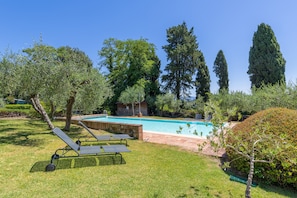 Une piscine entourée d’une pelouse, de chaises longues et d’arbres.