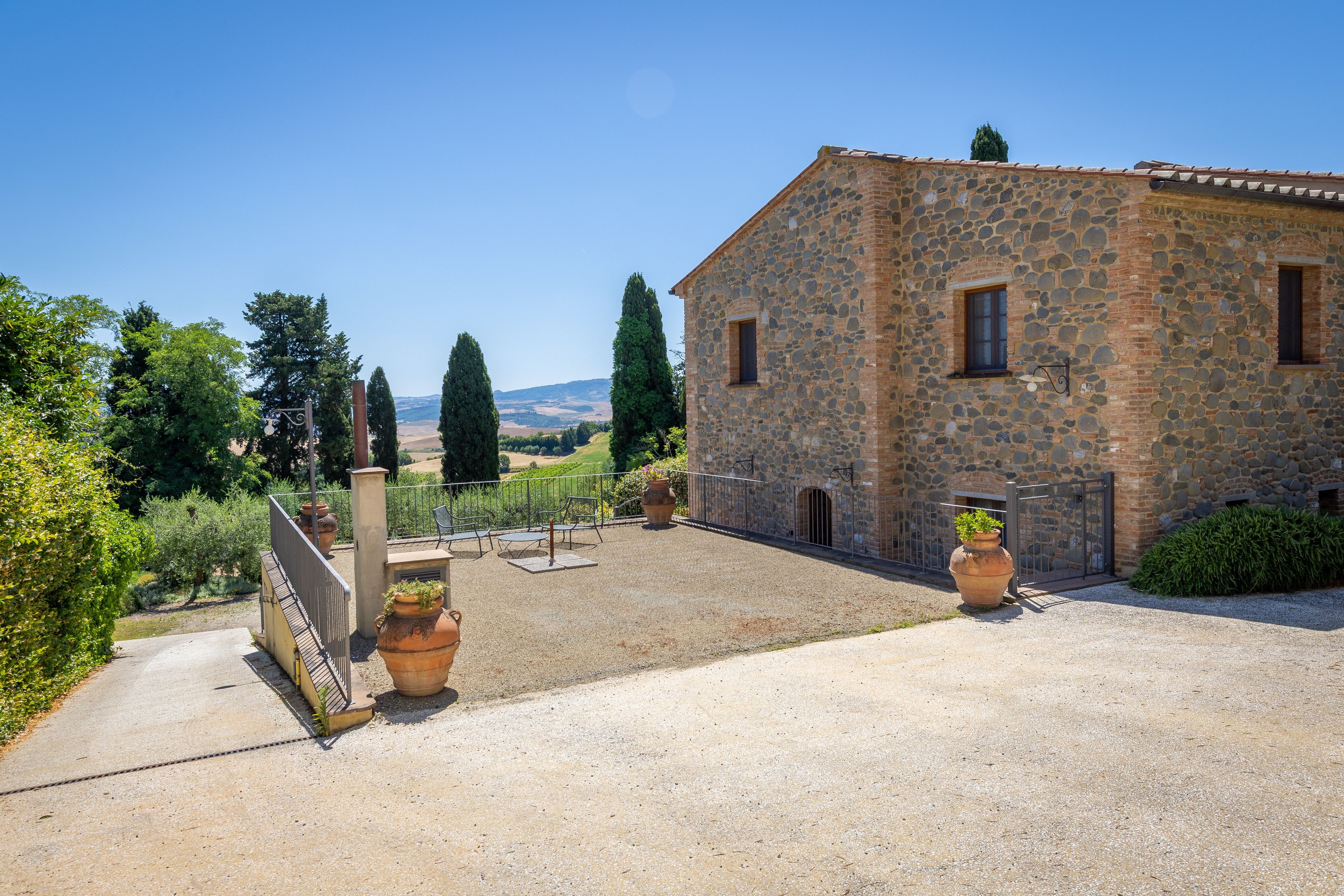 A stone building with a gravel courtyard, a gate, and potted plants.