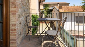 A balcony with a metal table and two chairs, a brick wall, and a tiled roof in the background. - Apartment 'Rosmarino' with Shared Pool, Garden, and Wi-Fi (Laiatico)