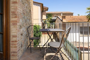 Un balcon avec une table en métal et deux chaises, un mur en briques et, au fond, un toit recouvert de tuiles.