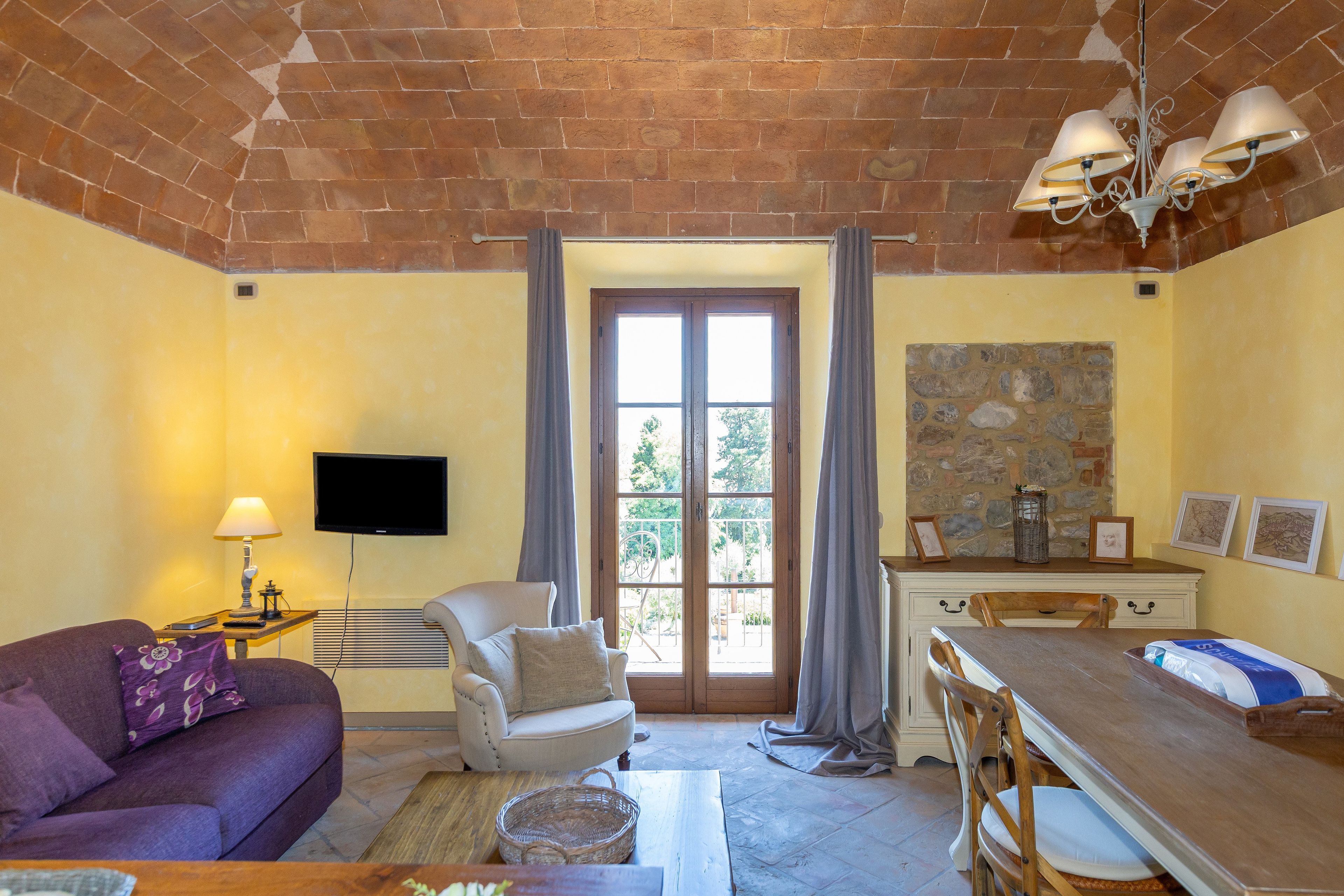 A furnished room with a sofa, armchair, dining table, and a television.