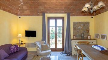 A furnished room with a sofa, armchair, dining table, and a television.