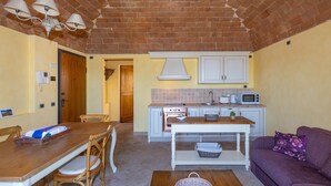 A compact kitchen with a brick ceiling, white cabinets, a microwave, and a dining area with a wooden table and chairs.
