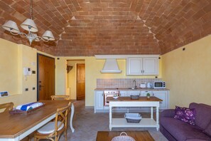 A compact kitchen with a brick ceiling, white cabinets, a microwave, and a dining area with a wooden table and chairs.