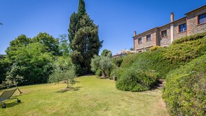 A well-maintained garden with a variety of trees and shrubs, a clear pathway, and a stone building with multiple windows.