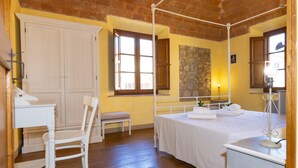 A bedroom with a four-poster bed, a chair, a desk with a lamp, and a wardrobe. - Apartment 'Rosmarino' with Shared Pool, Garden, and Wi-Fi (Laiatico)