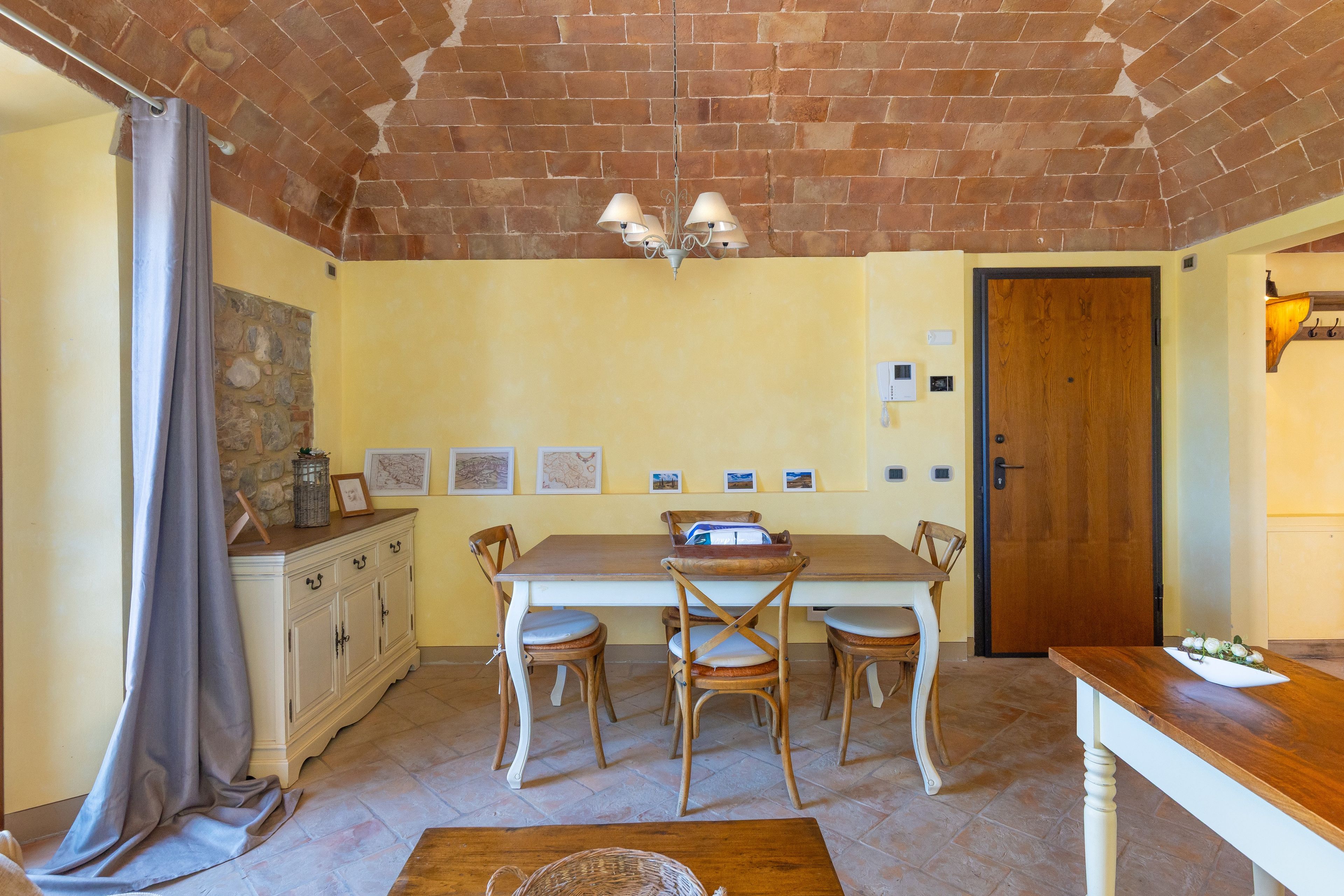 A dining area with a brick ceiling, a table with chairs, a wooden cabinet, and a door.
