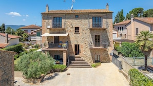 A two-story stone building with a balcony, a staircase leading to the entrance, and a clear view of the surrounding neighborhood. - Apartment 'Rosmarino' with Shared Pool, Garden, and Wi-Fi (Laiatico)