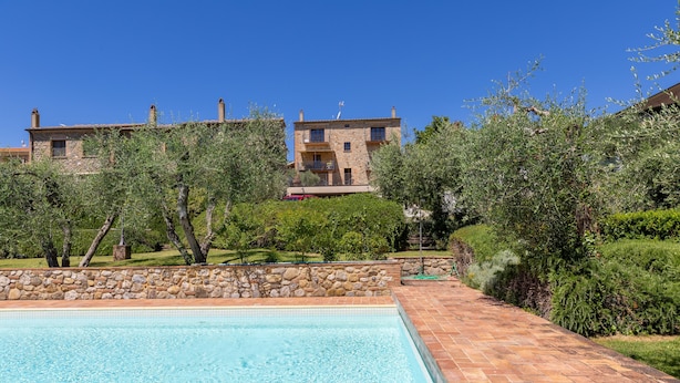 A swimming pool with a stone border, surrounded by a garden with various plants and a stone wall. - Apartment 'Rosmarino' with Shared Pool, Garden, and Wi-Fi (Laiatico)