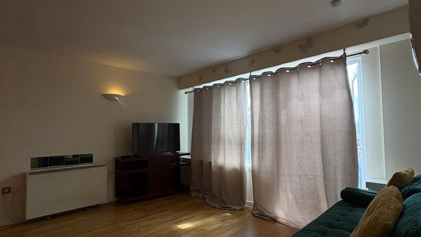 Een woonkamer met een groene bank, een televisie, een radiator en een raam met gordijnen.
