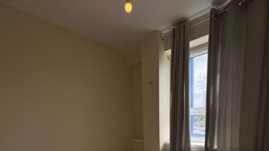 Een kleine kamer met een enkel bed, een raam, een nachtkastje en een plafondlamp.