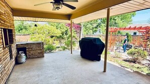 Ein überdachter Patio-Bereich mit Deckenventilator, Grill und Backsteinmauer.