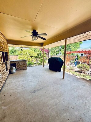 Ein überdachter Patio-Bereich mit Deckenventilator, Grill und Backsteinmauer.