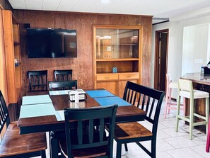 A dining area with a wooden table, chairs, a television mounted on the wall, and a cabinet with glass doors. - 17th Street Inn-Pawhuska (Pawhuska)