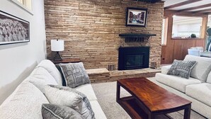 Ein Wohnzimmer mit Steinwand, Kamin und zwei Sofas mit gemusterten Kissen.