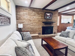 Ein Wohnzimmer mit Steinwand, Kamin und zwei Sofas mit gemusterten Kissen.