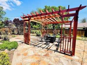 Un patio couvert doté d’une pergola, d’un revêtement de sol en pierre et de mobilier d’extérieur.
