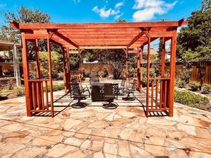 Une terrasse extérieure couverte, dotée d’un sol en pierre et d’une structure en bois formant une pergola.