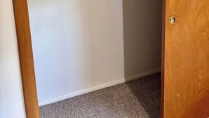 Ein Schrank mit weißer Tür, einem Holzrahmen und einem Einlegebrett mit gefalteter Kleidung.