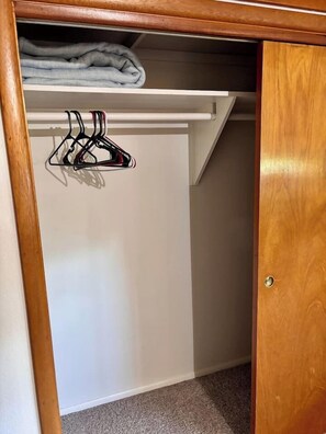 Ein Schrank mit weißer Tür, einem Holzrahmen und einem Einlegebrett mit gefalteter Kleidung.