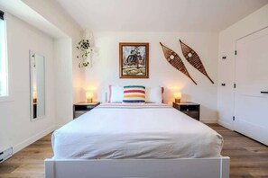 A bedroom with a large bed, bedside tables, a mirror, a framed picture, and two wall hangings. - The Point Lodge | Cozy Invermere Getaway (Invermere)