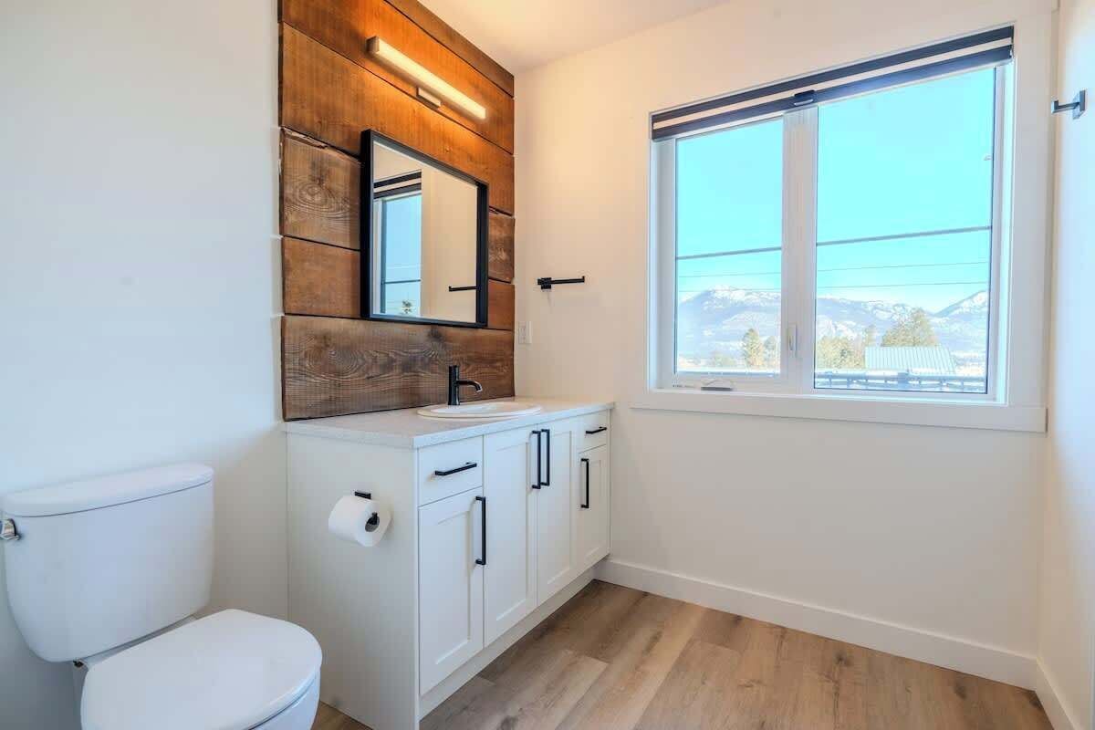 Une salle de bain comprenant des toilettes, un lavabo avec des placards, un miroir et une fenêtre donnant sur un paysage agréable.