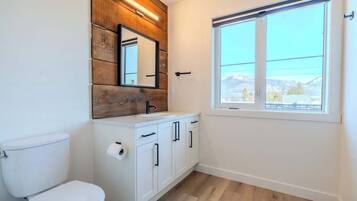 Une salle de bain comprenant des toilettes, un lavabo avec des placards, un miroir et une fenêtre donnant sur un paysage agréable.