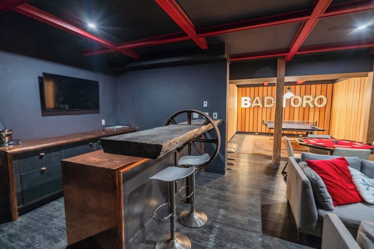 A modern bar area with a bar stool, a counter, and a seating area with a sofa and chairs.