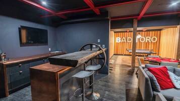 A modern bar area with a bar stool, a counter, and a seating area with a sofa and chairs.