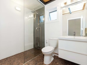 A modern bathroom with a glass-enclosed shower, a white toilet, and a vanity with a mirror. - The City Haven | Sleeps 4 | (Calgary)