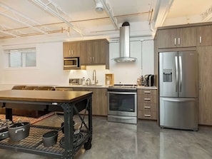 A modern kitchen with stainless steel appliances, wooden cabinets, and a central island. - The City Haven | Sleeps 4 | (Calgary)