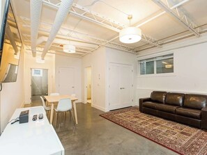 A spacious room with a white table, chairs, a brown leather sofa, and a patterned rug. - The City Haven | Sleeps 4 | (Calgary)