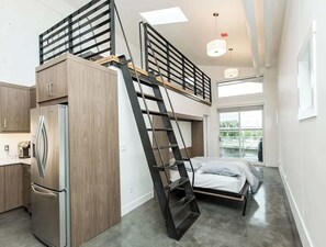 Een compact appartement met kitchenette, een bed, een slaapkamer op een entresol en een trap.
