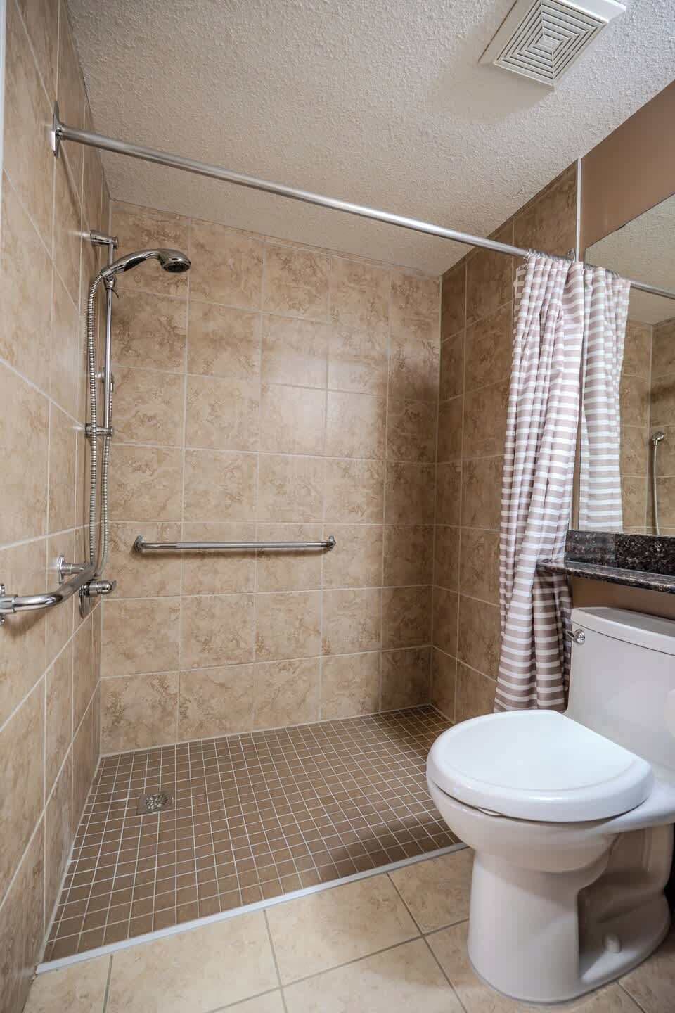 A bathroom with a shower, grab bar, toilet, and a striped shower curtain.