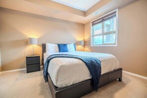 A bedroom with a bed, bedside tables, lamps, and a window. - Valley View Haven | BBQ, Hot Tub, Pool,Gym | (Invermere)