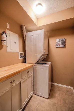A laundry room with a washing machine, a dryer, a wooden counter, a fire extinguisher, and a small picture on the wall. - Valley View Haven | BBQ, Hot Tub, Pool,Gym | (Invermere)