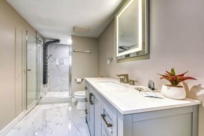A modern bathroom with a glass shower enclosure, a white marble floor, and a large mirror above the vanity. - Backyard Oasis - Hot Tub, BBQ, Outdoor Bar (Invermere)