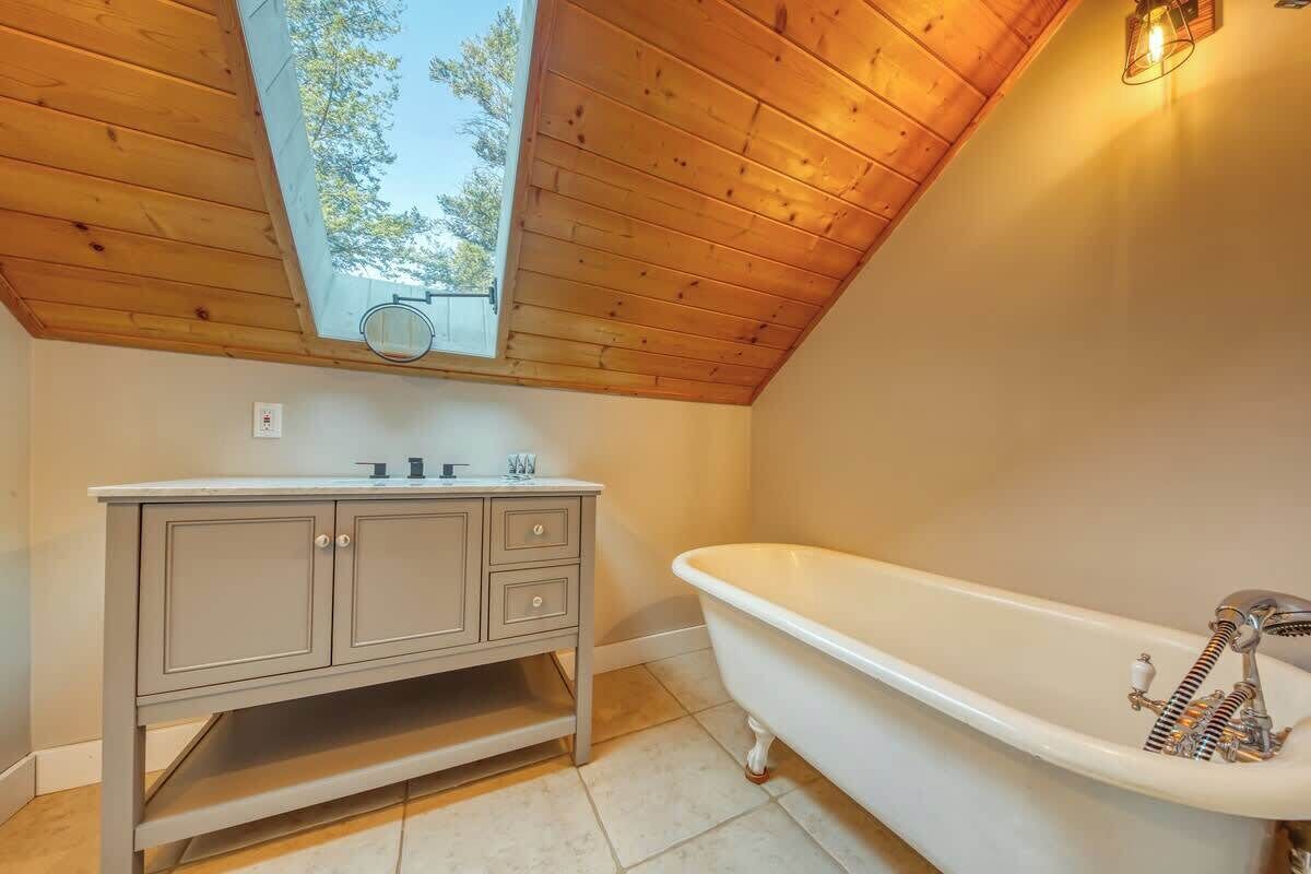 Een badkamer met een houten plafond, een wastafelmeubel met kastjes, een bad en een dakraam.