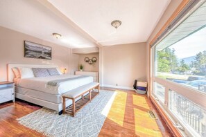 A bedroom with a bed, bedside tables, a bench, a rug, a window, and a view of the outside. - Backyard Oasis - Hot Tub, BBQ, Outdoor Bar (Invermere)